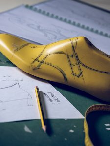 Shoe last placed near pencil and paper footwear design draft